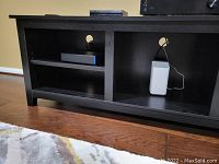 Front view of the black wooden entertainment stand with multiple compartments and cable management holes