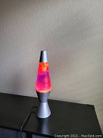 Lava lamp placed on a black surface with wax blobs floating inside, showing orange and purple colors under natural light.