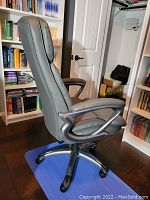 Side view of gray cushioned office chair showing padded armrests, metal swivel base, and caster wheels.