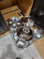 View of the steel pots, pans, pressure cooker, idli steamer, and bowls in drawer rack.
