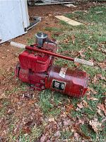 Full view of Sears Model 2650 alternator showing red metal body and control knob on top, placed on the ground with grass and leaves.