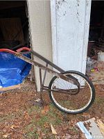 Full view of antique garden tiller showing wooden handle and metal frame with large bicycle tire wheel.