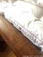 Close up of white Tommy Hilfiger down bed topper showing logo and fabric.