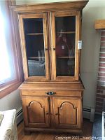 Front view of the wooden cabinet showing glass doors, drawer, and lower cabinet doors with panel design