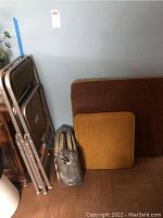 Folded table, two folding chairs stacked together, two seat cushions leaning against the wall, view from a distance