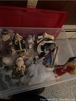 Clear view of multiple Santa figurines in a plastic storage bin with white stuffing filler.