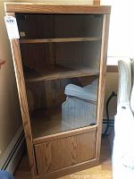 Front view of wooden electronics cabinet with glass door showing two interior shelves and bottom compartment