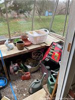 Full view of garden pots, watering cans, Toro leaf blower box, hedge trimmer and other garden tools organized on a greenhouse shelf.