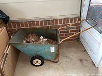 Full side view of the blue metal garden cart with rust and debris inside.