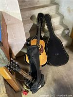 Two guitars leaning against basement steps: acoustic in hard case and black electric in gig bag