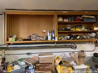 Wooden wall-mounted cabinet with shelves holding assorted hardware and household items, boxes, cans, and small tools.