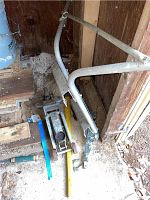 Overview of the lot showing hydraulic car jack, blue hand winch, and silver ladder stabilizer leaning in corner of wooden shed.