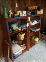 Front view of two matching wood bookcases filled with various personal and household items (not included in lot) in a wood-paneled room.