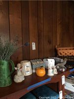 Full overview of the lot arranged on a wood shelf showing the various decorative ceramics, pottery, figurines, and basket.