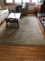 Large beige 9'x6' area rug with subtle woven leaf pattern, placed in living room under coffee table, showing wear but intact.