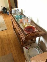 Photo showing side view of wooden sofa table with decorative carved edge and turned legs, items on table not included.