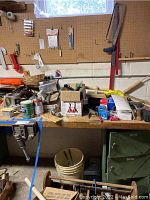 Full overview of the workbench with assorted tools, boxes, cans, and baskets scattered on the surface and pegboard behind.