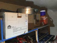 Shelf with stacked cardboard boxes and metal pots on the top shelf, showing part of storage and items included.
