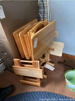 Photo showing three wooden TV trays stacked in a wooden stand with foldable legs.