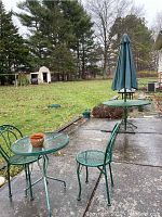 Patio with green wrought iron table set including umbrella and two chairs on concrete patio with lawn in background