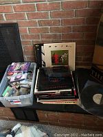 A photo showing a plastic bin filled with cassette tapes and DVDs beside a stack of vinyl records.