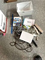 Overview of all included items in the lot on carpeted floor including console, controllers, sensor bar, cables, game case and manual.
