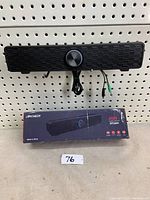 Front view of the black Archeer AS04 gaming computer soundbar speaker mounted on a pegboard with its cables hanging below and the product box placed underneath.