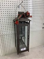 Front angle showing the tall rectangular metal lantern with glass panes, mirrored back, tea light holders inside, and a plaid bow tied to handle.