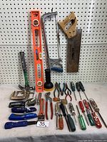 Full lot showing various hand tools including saws, levels, screwdrivers, pliers, utility knives and clamps arranged on a pegboard and bench surface.