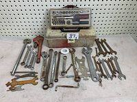 Tools spread on surface including wrenches, adjustable wrenches, pipe wrenches, and two metal toolboxes in background.
