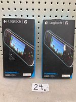 Two Logitech Powershell controller boxes hung on pegboard with number 24 tag. Both boxes black with product photo on front showing in-use controller with game screen.