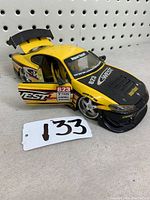 Side view of the yellow Nissan Silvia model car with driver-side door open revealing interior details. Car features sponsor decals and black hood.