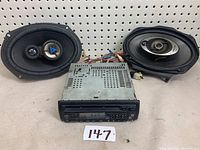 Front view of a Kenwood car CD player with two oval speakers and wiring included. Unit and speakers show some wear and tear.