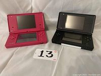 Both Nintendo handheld consoles shown side by side on cloth background with lot tag visible