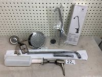 Lot items displayed against pegboard including rainfall shower head, chrome pipes, water faucet, soap dispenser, and hoses.