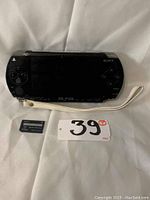 Black Sony PSP gaming console with screen and buttons visible, white wrist strap attached.