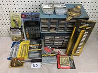 Wide shot of tool and hardware lot showing storage bin, calculator, brass hardware, Duramax drill bits, screws, nails, packaging details