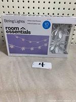 Box front showing Room Essentials branding and photo of the white metal flower string lights with 10 lights arranged on string, designed for indoor/outdoor use.