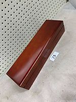 Top view of a rectangular closed wooden tea box placed on the floor near a pegboard wall, showing the smooth polished finish and the lid edges.