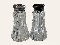 Pair of cut crystal salt and pepper shakers with sterling silver tops, clear crystal bodies with vertical cut facets, shown against neutral background.