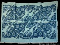 Full view of light blue fabric square with dark blue floral pattern and fringe edges spread flat.