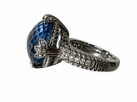 Close-up side angle showing checkerboard faceted blue topaz center stone with sterling silver prongs and accent stones on band.
