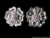Close-up of pair of sterling silver floral earrings with pink stone centers on black background
