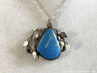 Close-up of a sterling silver necklace pendant with a large turquoise stone, accented by silver leaves and freshwater pearls.