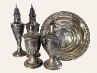 Front view of four silver salt and pepper shakers with pedestal compote behind
