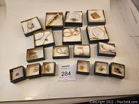 Full lot of 17 Avon jewelry pieces in blue and gold tone boxes, including necklaces, bracelets, pins, brooches, locket, earrings.