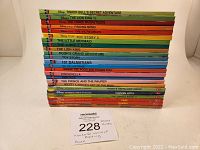 Stack of 24 Disney World of Reading books showing colorful spine titles including Tinker Bell, Lion King, The Three Musketeers, Finding Nemo, The Incredibles, Toy Story 2, and more.
