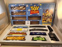 Full view of the boxed Disney Toy Story Express HO scale electric train set including train cars, track pieces, controller in original tray packaging with collector's box shown in background.