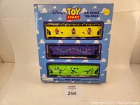 Front of boxed Disney Toy Story HO Scale Tri-Pack Train Cars with visible three themed train cars inside windows: yellow Mr. Potato Head, purple with lights, green Rex car.
