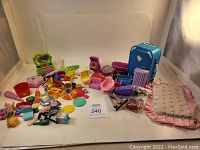 Wide view of various small doll furniture pieces, beauty tools, mini suitcases, and accessories laid out on a white surface.